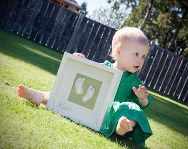 Little girl sitting in her backyard with the little feet Memory Castings Shadowbox she made as a newborn baby